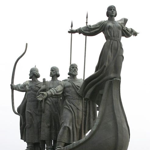 Bronze statue of figures on a boat with a woman at the front, set against a plain background.