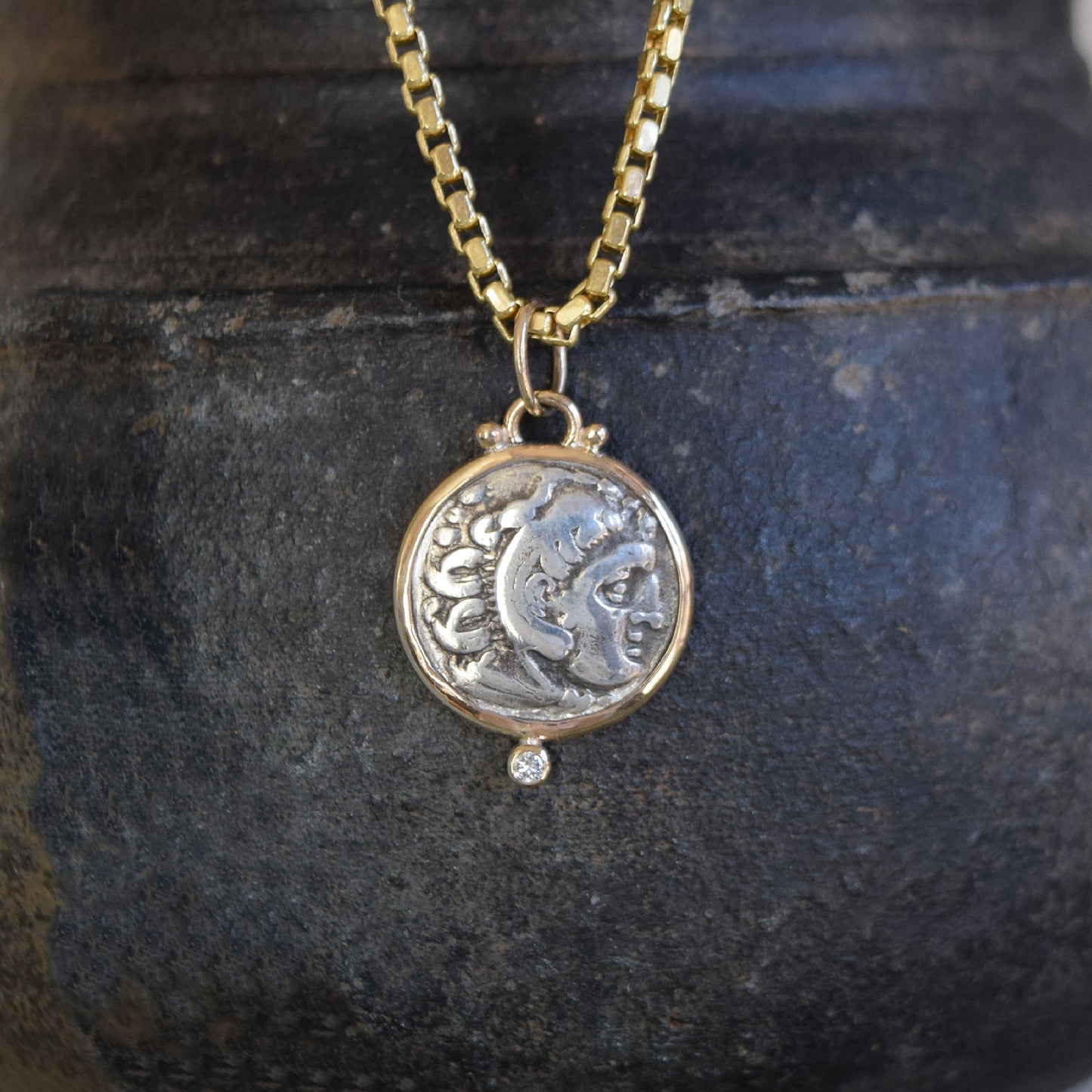 Necklace with an ancient coin and diamond pendant on a dark stone surface