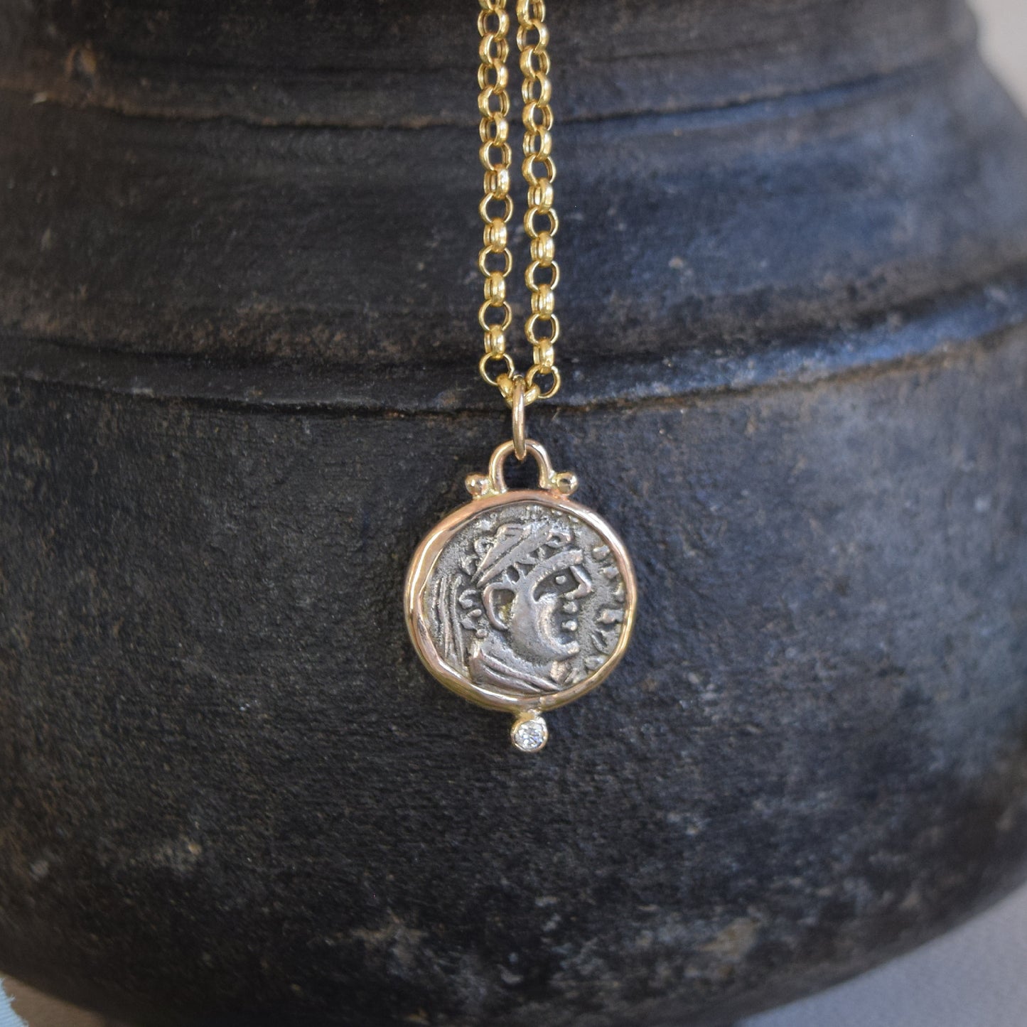 Gold necklace with ancient coin pendant with diamond on a dark textured surface